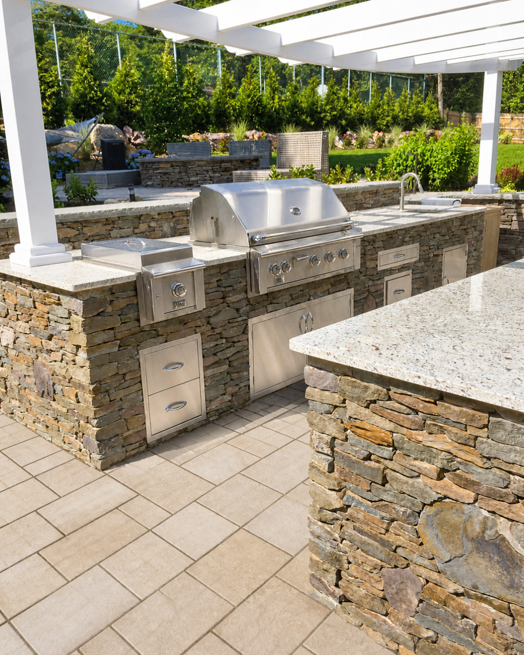 Stone outdoor kitchen with stainless grill beneath a white pergola