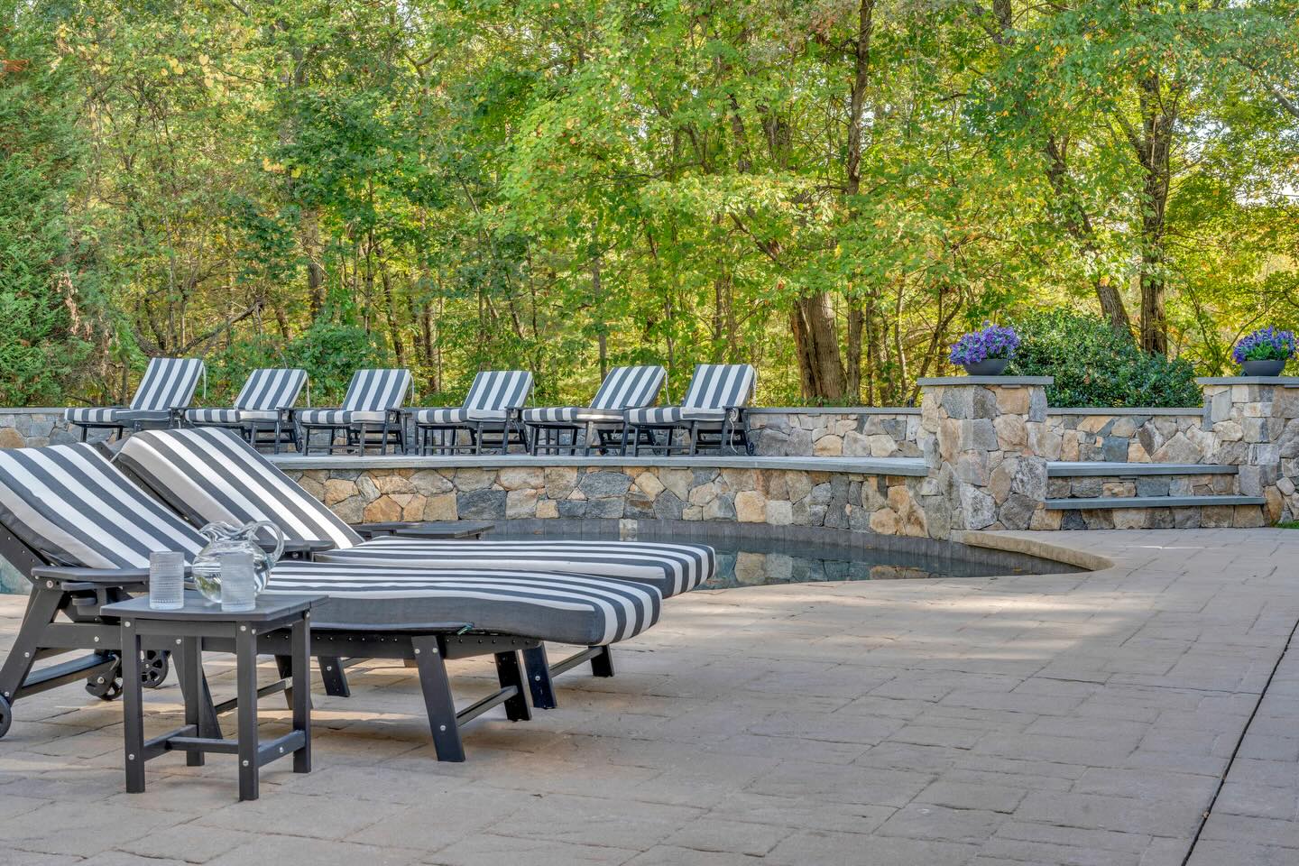 Custom pool deck with natural stone retaining wall and lounge seating built by Precision Excavation in Foxborough, MA