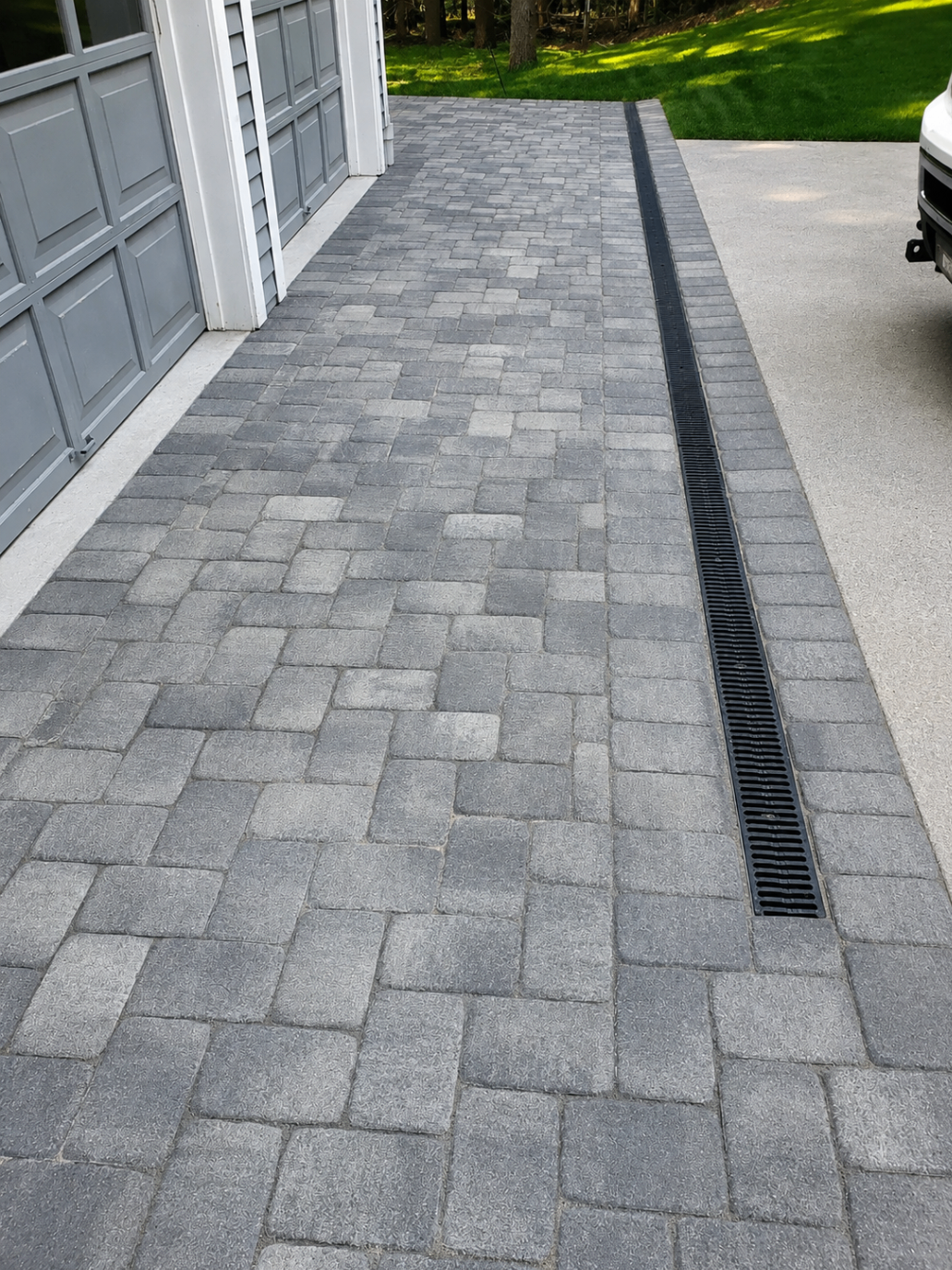 Paver driveway apron with integrated black channel drain running beside a garage
